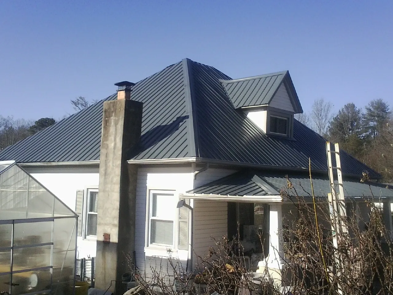 Dark blue standing seam metal roof on a white farmhouse with dormer — Slate & Tile Roof Repair by Roofing Brothers in Swink