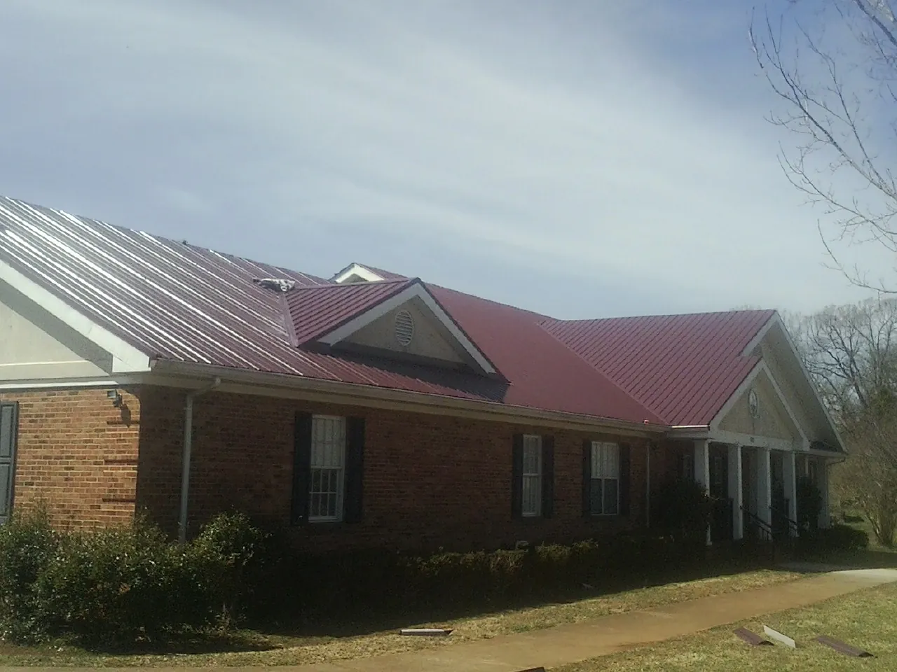 Red metal roof with gabled entries on a long brick building, from a Hail Damage Roof Repair job in Swink