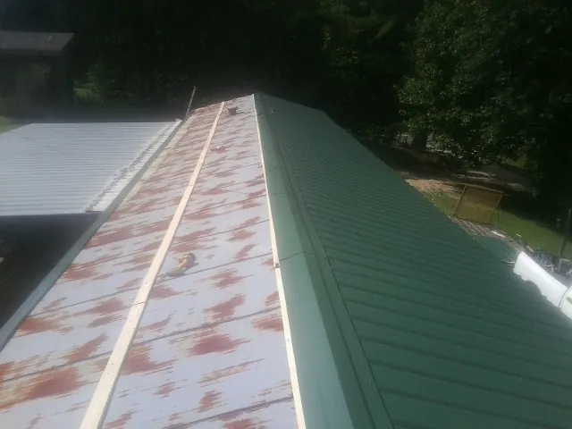 Old rusted panels beside newly installed green metal roofing — Wind Damage Roof Repair by Roofing Brothers in Swink