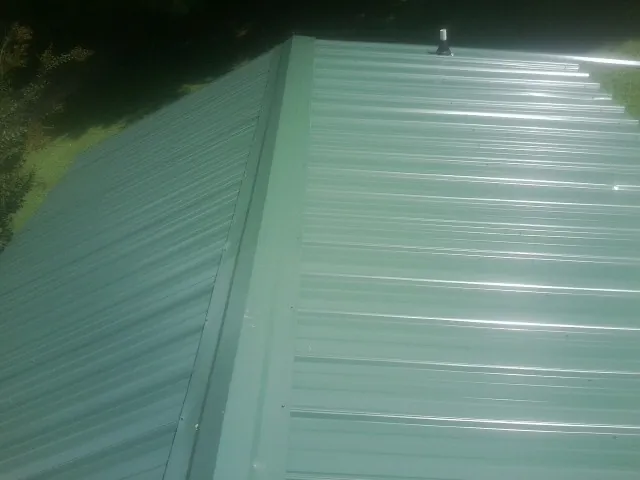 New green metal panels meeting at the ridge of a roof — Flat Roof Repair work by our crew in Swink