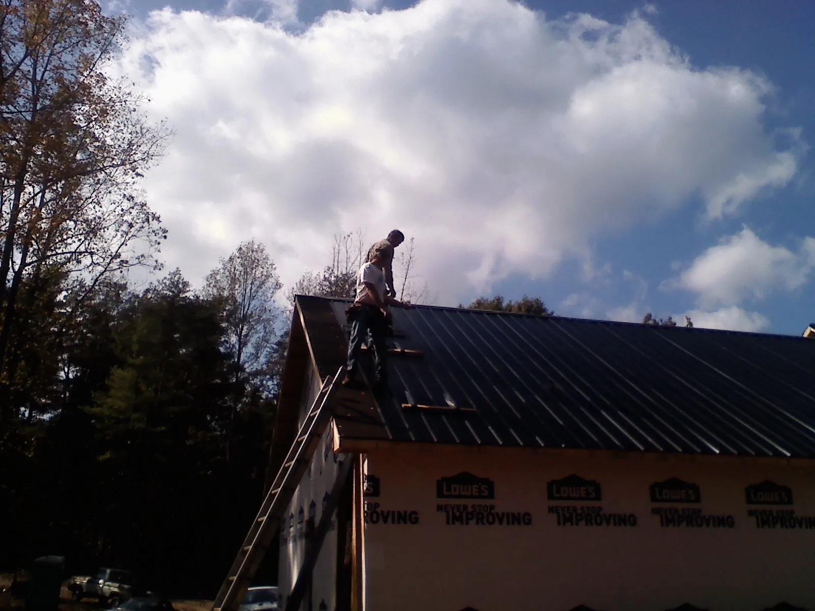 Roofer fastening dark metal panels high against a cloudy sky, from a Roof Inspection job in Swink