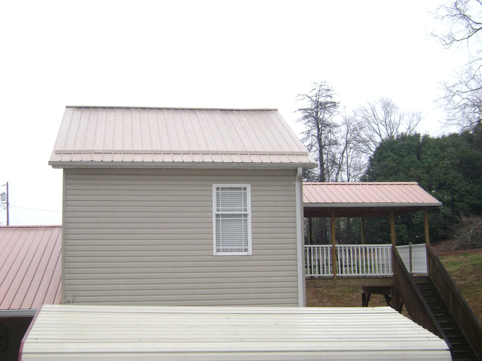 Tan metal roofs on a two story addition and attached porch, from a Roof Replacement job in Swink